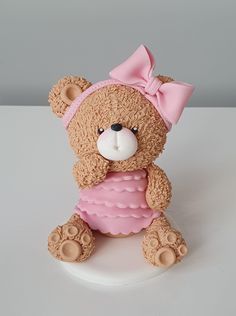 a brown teddy bear with a pink bow on it's head sitting on a white surface