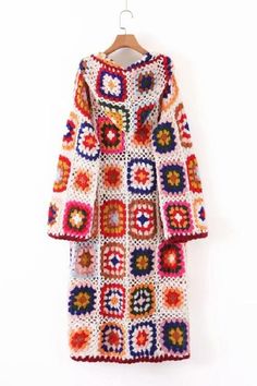 a crocheted coat hanging on a hanger next to a white wall with an orange, red, and blue pattern