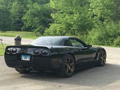 a black sports car is parked on the side of the road in front of some trees