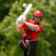 a female cricket player is swinging her bat at the ball while wearing red and black