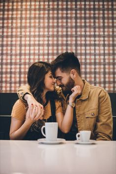 a man and woman sitting next to each other in front of two coffee mugs