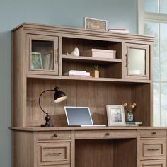 a wooden desk with a laptop on top of it next to a book shelf and window