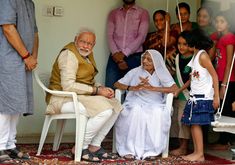 an old woman sitting in a chair with other people standing around her and on the ground