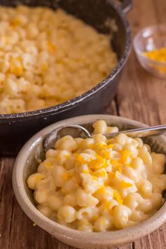 macaroni and cheese in a bowl next to a skillet on a wooden table