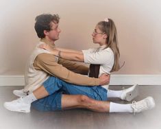 a man and woman sitting on the floor with their arms around each other's shoulders