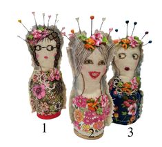 three dolls made out of fabric with flowers on their heads and hair pins in the middle