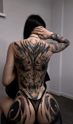 a woman with tattoos on her back sitting in a chair