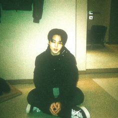 a young man sitting on the floor in front of a mirror with his hands crossed