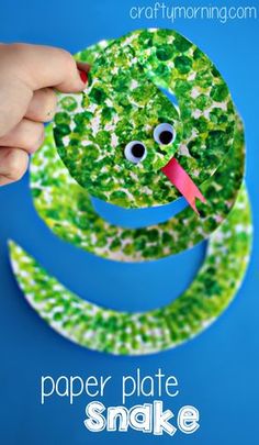 a child's hand holding up a paper plate with a green snake on it