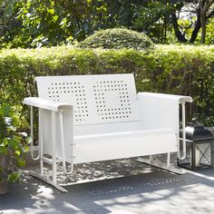 a white park bench sitting next to a bush