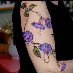 a woman's arm with purple flowers and green leaves on the left side of her arm