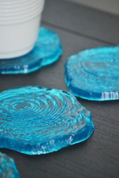 three blue coasters sitting on top of a wooden table next to a white cup