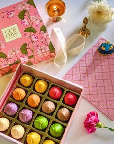 a pink box filled with assorted chocolates on top of a table next to other items