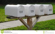 three white mailboxes on a wooden post in front of a sidewalk and grass