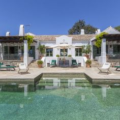 an outdoor swimming pool with lounge chairs and umbrellas next to a house in the background