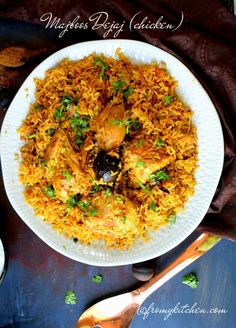 a white plate topped with chicken and rice next to a spoon on a tablecloth