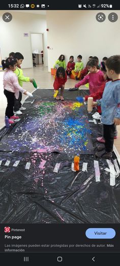 some kids are painting on a large sheet of black paper with colored paint and watercolors