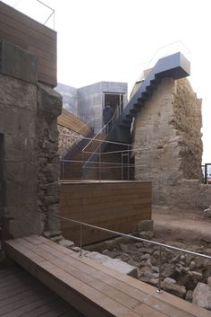 a wooden bench sitting in front of a stone building next to a stair case with glass railings