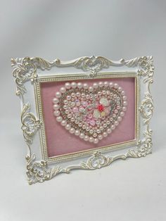 a pink and white frame with pearls in the shape of a heart on it's side