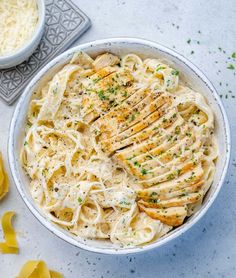 a white bowl filled with chicken alfredo pasta and parmesan cheese on the side