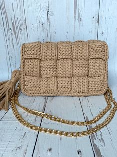 the beige knitted clutch purse with tasselled handles and gold chain is sitting on a white wooden surface