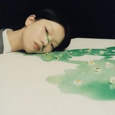 a woman laying on top of a bed with her head resting on the table next to flowers