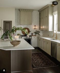 a large kitchen with white cabinets and an island in the middle is decorated with potted plants