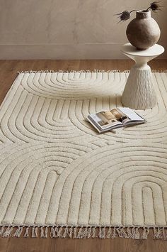 a white rug with fringes and a vase on the floor in front of it