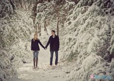 two people holding hands in the middle of a snow covered path with trees on both sides