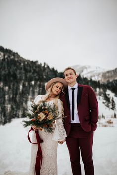 a bride and groom standing in the snow with their arms around each other, holding bouquets