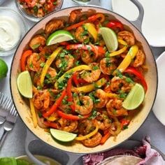 a skillet filled with shrimp, peppers and limes on top of a table