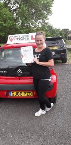 a woman standing next to a red car holding up a paper with writing on it