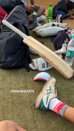 a baseball bat laying on the ground next to shoes and water bottles with people sitting around it