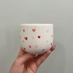 a hand holding a white bowl with hearts painted on the outside and inside, in front of a gray background