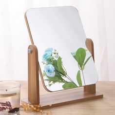 a mirror sitting on top of a wooden table next to a jar of tea and flowers