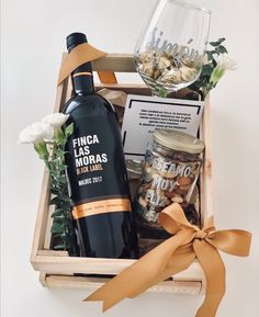 a bottle of wine in a wooden box next to a glass and some flowers on a table