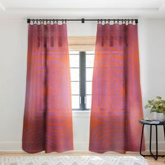 an orange and pink curtain hanging in front of a window with a white rug on the floor