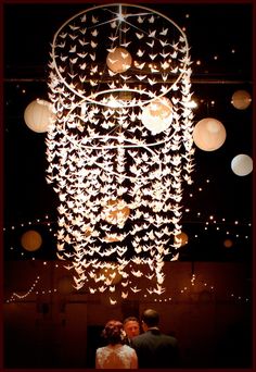 a bride and groom standing under a chandelier with paper birds hanging from it