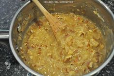 a wooden spoon in a metal pot filled with yellow colored food and sauce on top of a granite countertop