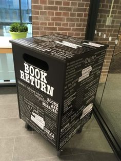 a book return box sitting in front of a brick wall with glass doors on it