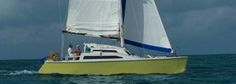 a yellow sailboat with people on it in the middle of the ocean under a cloudy sky