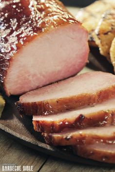 sliced ham on a plate with crackers next to it and another piece of meat in the background