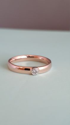 a rose gold ring with a single diamond on the front and side, sitting on a white surface