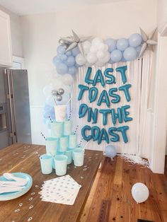 a table with balloons, plates and cups on it in front of a wall that says last toast on the coast