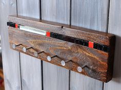 a coat rack made out of wood with red and black strips on the sides, hanging from a wooden wall