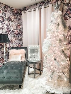 a white christmas tree sitting in front of a window next to a couch and chair