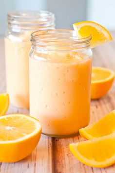 two mason jars filled with orange smoothie on top of a wooden table next to sliced oranges