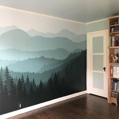 a room with a book shelf and painted mountain scene on the wall next to a bookshelf