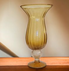 a yellow glass vase sitting on top of a wooden table next to a lamp shade