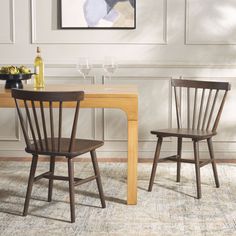 two wooden chairs sitting at a table with wine glasses on it and a painting hanging above the table